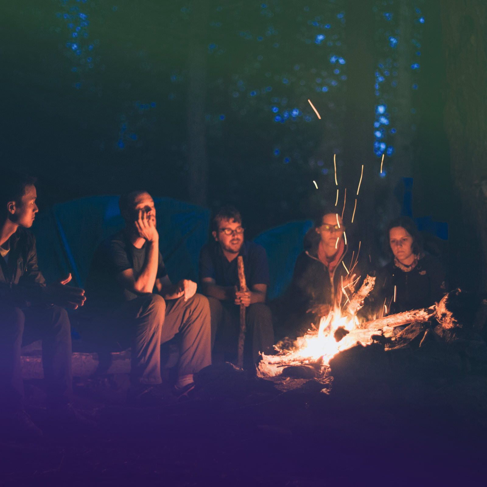 Bild von einer Gruppe von Menschen, die gemeinsam am Lagerfeuer sitzen.