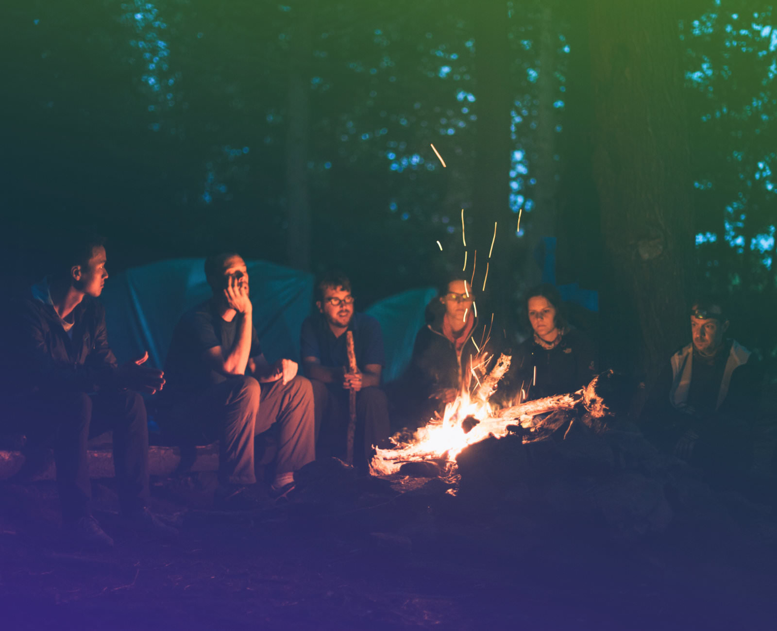Bild von einer Gruppe von Menschen, die gemeinsam am Lagerfeuer sitzen.